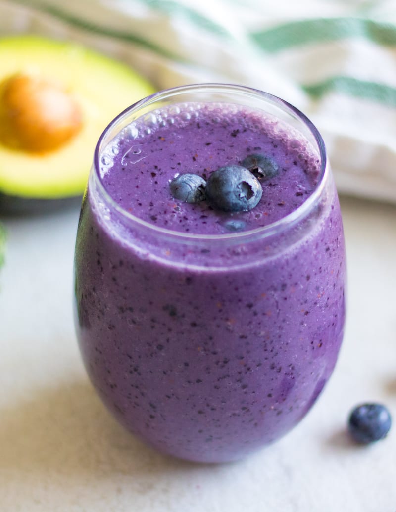 Blueberry Smoothie in glass with avocado and blueberries in background